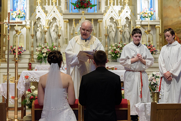 Bride and groom kneeling before the priest doing a blessing, Catholic Wedding Ceremony.